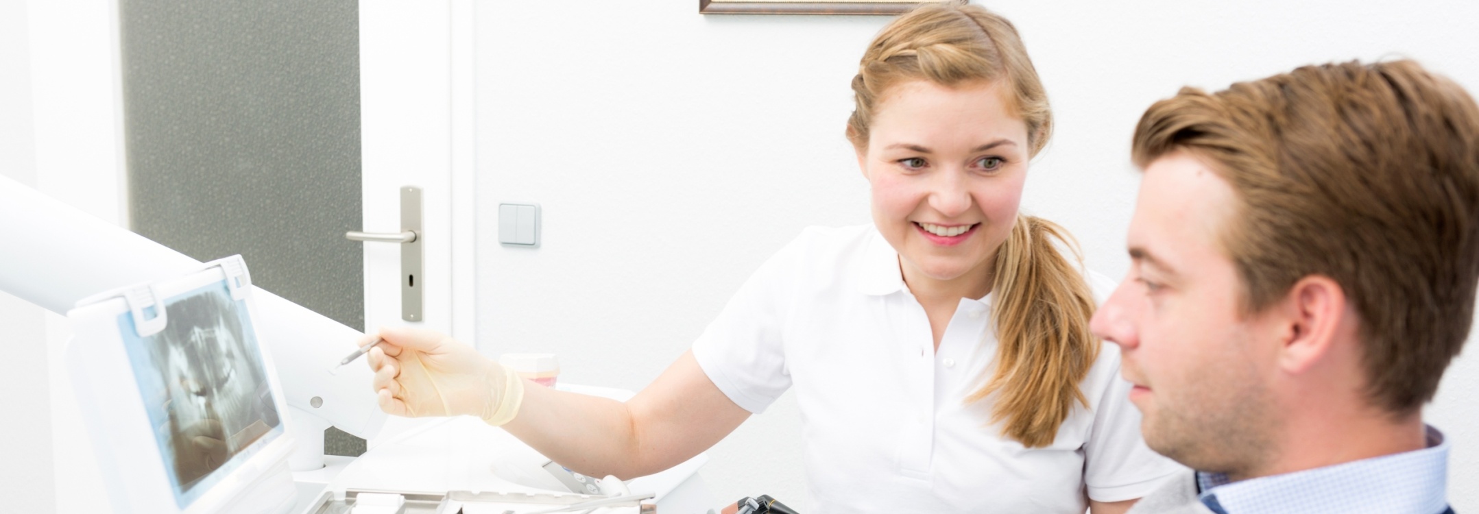 Intro Photo: Zahnärztin zeigt einem sitzenden Patienten ein Röntgenbild auf dem Bildschirm und erläutert die Befunde in einem hellen Behandlungszimmer