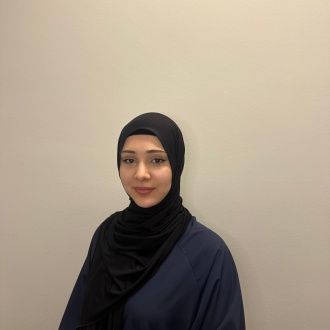 Porträt von Auszubildender Rayana Lorsanova aus DIE ZAHNARZTPRAXIS Stralsund, im dunkelblauen Kasack und schwarzem Kopftuch vor hellem Hintergrund, freundlich zur Kamera gewandt.